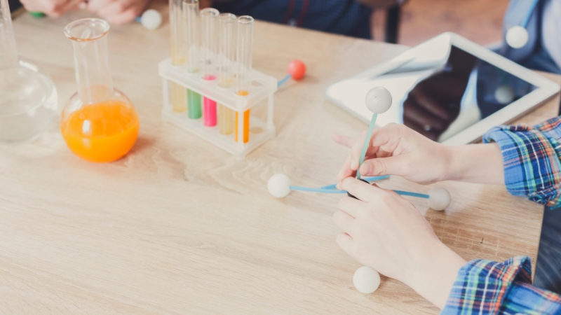 Deca sede za stolom i koriste jednostavne laboratorijske posude i modele molekula tokom kućnih eksperimenata iz fizike