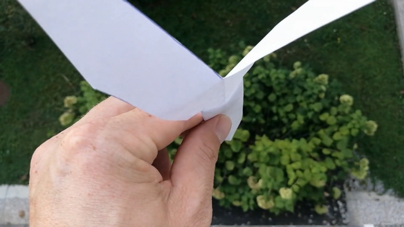 Osoba drži papirni helikopter u vazduhu na prozoru