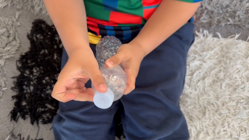 Dete drži uvrnutu flašu i odvrće čep, dok izvodi Pop Bottle eksperiment iz fizike