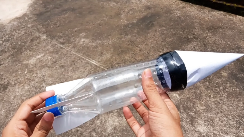 Ruka drži plastičnu bocu pretvorenu u vodenu raketu sa papirnim vrhom i repnim stabilizatorima